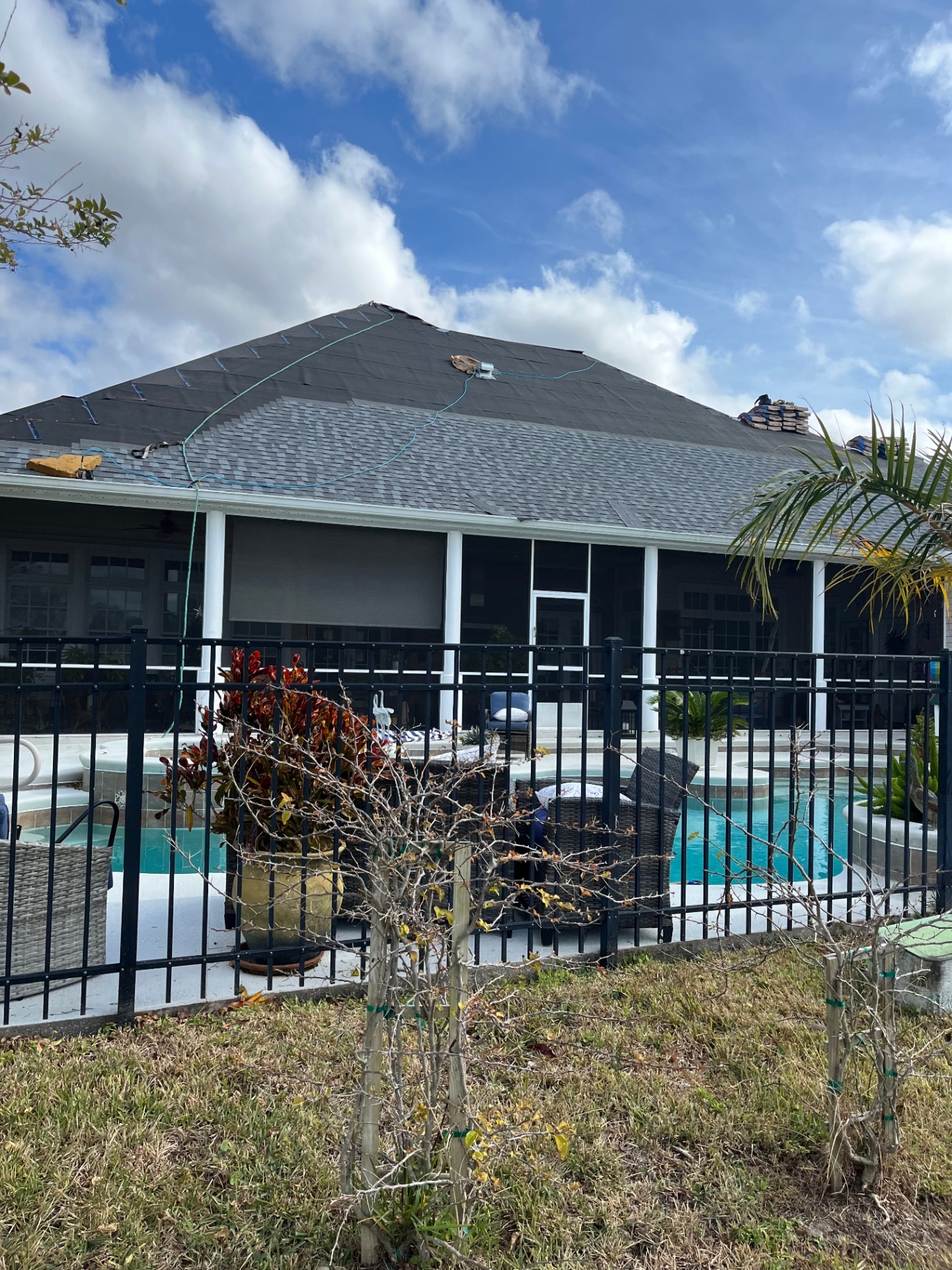 Shingle roof replacement in progress on a Florida pool home — underlayment installed with new shingles being loaded