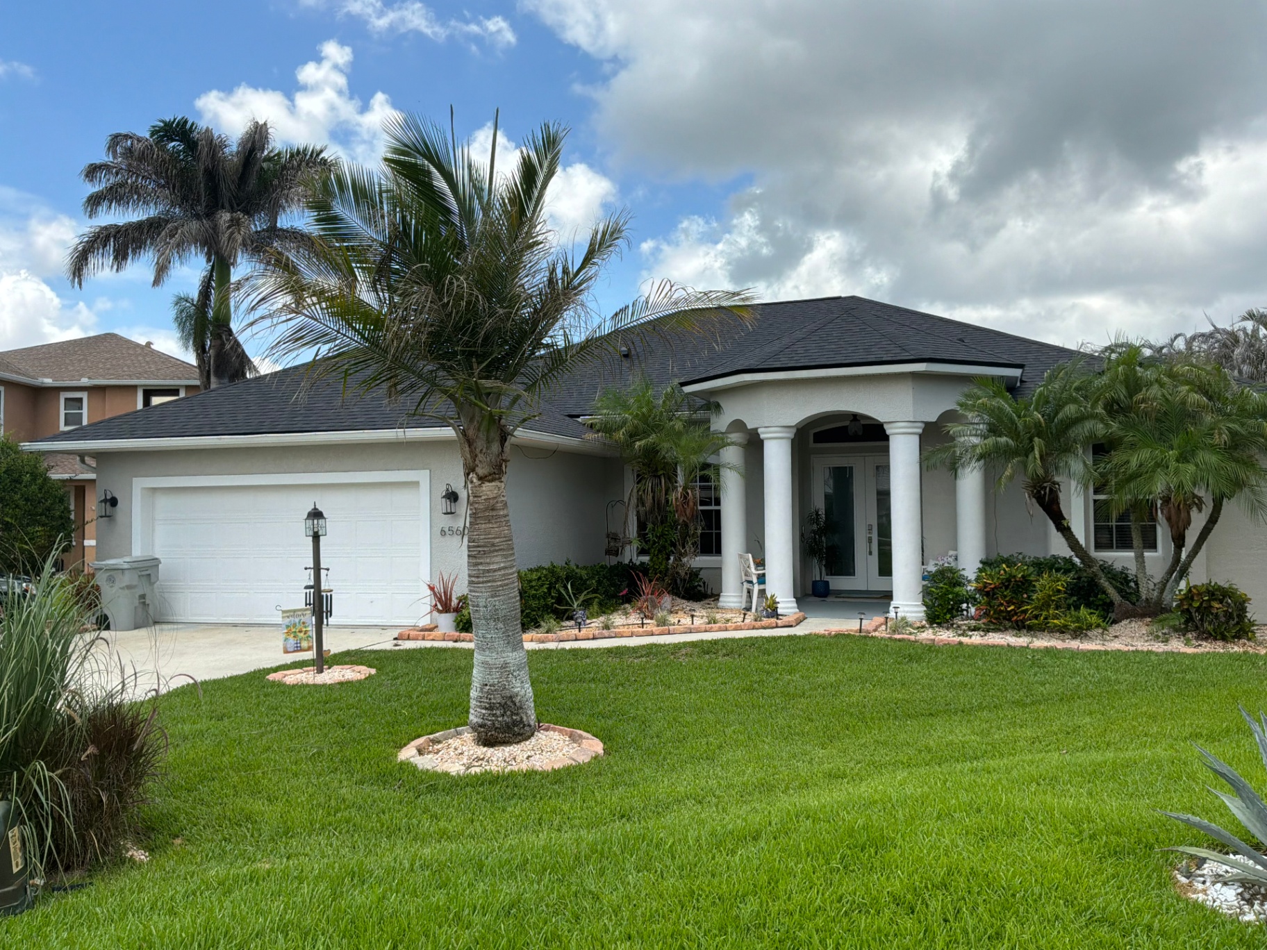 Completed dark architectural shingle roof on a Florida home with columned entry and palm trees