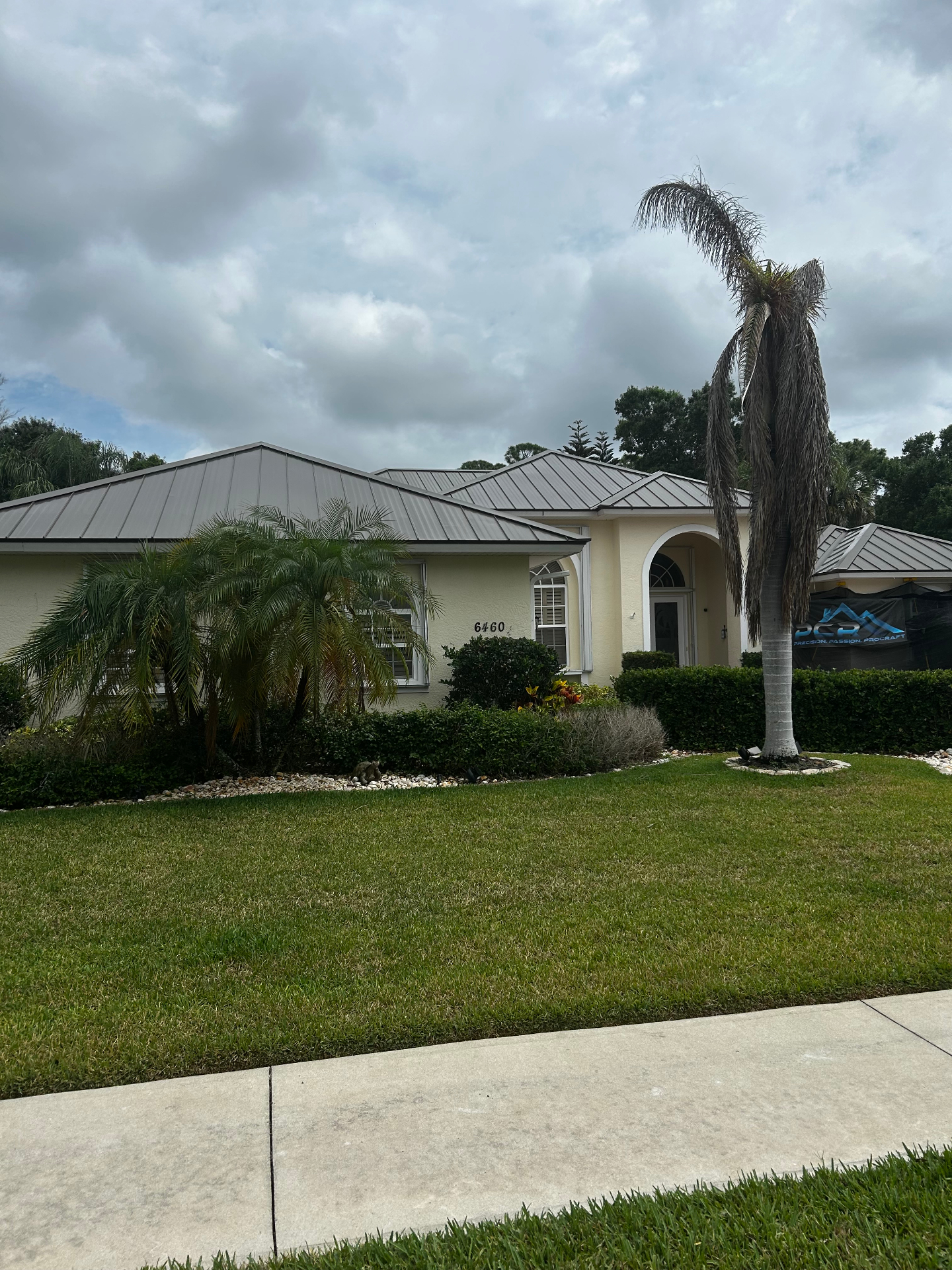 Standing-seam metal roof on a yellow Florida home with ProCraft jobsite banner